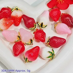 Close-up of colorful strawberry charms with golden leaf loops for DIY jewelry projects