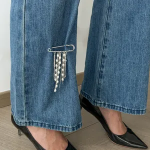 Close-up detail of silver safety pin brooch with faux pearl tassel pinned on blue jeans