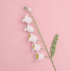 Detailed close-up of handmade white crocheted Lily of the Valley flower with green leaf.