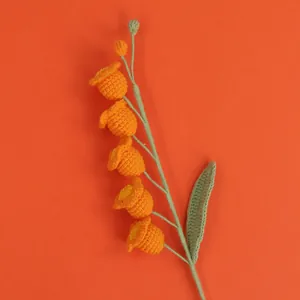 Close-up of a handcrafted orange crochet Lily of the Valley flower with fine yarn texture