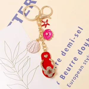 Detailopname van strand-sleutelhanger met teenslipper en schelpbedeltjes in goudkleur.