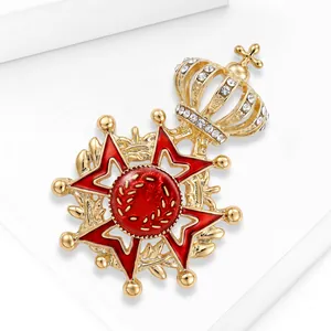 Close-up of elegant gold alloy crown brooch with red enamel and rhinestones.