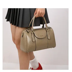 Close-up of a vintage khaki oil leather Boston pillow handbag held by a woman in a skirt.