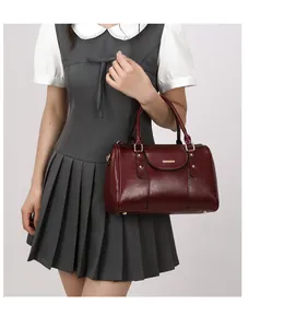 Detailed shot of a burgundy oil-wax leather Boston bag held by a model in a grey dress.