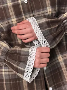 Macro view of vintage brown plaid shirt featuring elegant white lace cuffs and buttons