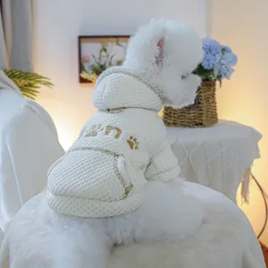Detail showing a white waffle-knit pet hoodie with gold paw embroidery and a D-ring