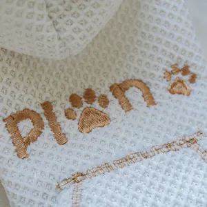 Close-up detail of white waffle knit pet hoodie featuring brown paw embroidery