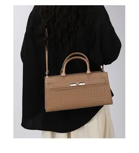 Vue arrière d'un sac à main tissé beige avec fermoir doré porté par un mannequin en chemise noire.