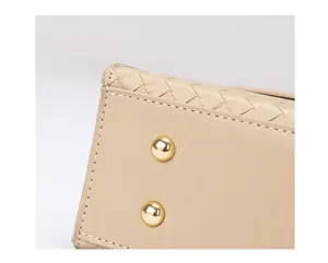 Vue détaillée d'un sac à main beige tissé avec des clous dorés et des coutures blanches