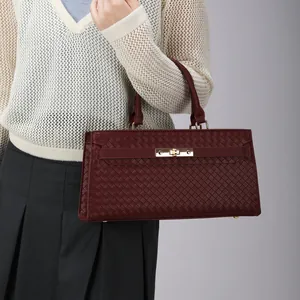 Sac à main bordeaux tissé élégant avec fermoir doré porté par un mannequin en pull tricoté.