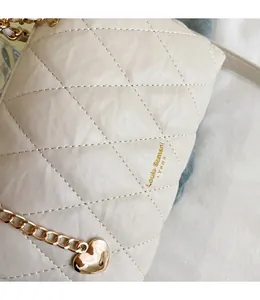 Detailopname van een crème gewatteerde tas met ruitpatroon en gouden hartjesketting