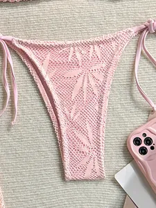 Gros plan sur le bas de bikini en crochet rose avec motifs floraux délicats et liens latéraux.