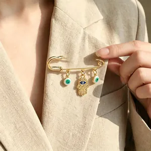 Detail of gold Hamsa Hand and Evil Eye charms on a safety pin brooch pinned to a blazer.
