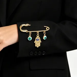 Macro view of gold safety pin brooch with textured Hamsa hand charm pinned to black fabric
