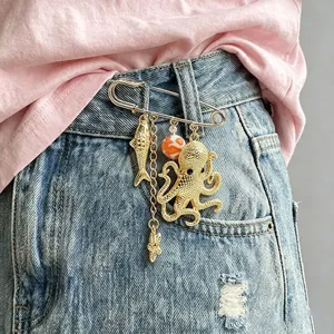 Detailed view of a gold ocean-themed brooch with octopus and fish charms on denim.