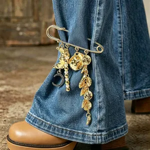 Detail shot of a vintage gold safety pin brooch with moon and pearl charms on denim jeans.
