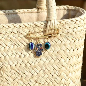 Macro view of gold Hamsa hand and blue Evil Eye charm brooch on woven straw bag