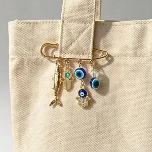 Detailed macro view of an Evil Eye and Hamsa hand charm safety pin brooch on a canvas bag