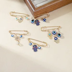 Close-up of gold safety pin brooches featuring blue evil eye and Hamsa hand charms.