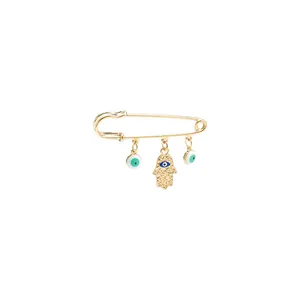 Macro detail view of a golden safety pin brooch with Hamsa Hand and Evil Eye charms