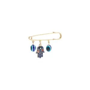 Close-up detail of gold safety pin brooch with blue evil eye and Hamsa hand charms