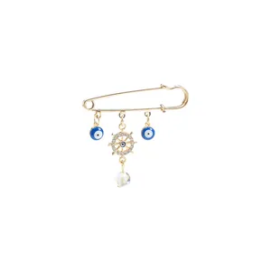 Detailed view of gold safety pin brooch with blue evil eye and crystal ship wheel charms