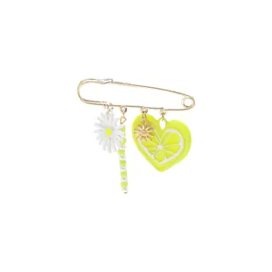 Detail view of yellow heart lemon slice and white daisy charms on a gold safety pin brooch