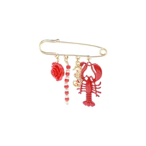 Detail view of the red lobster and seahorse charms on a golden safety pin brooch.