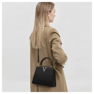 Back view of a woman wearing a tan coat holding a black structured luxury style handbag.