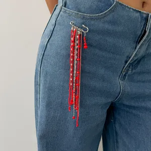 Vue détaillée d'une broche épingle de nourrice argentée avec perles rouges et chaînes sur jean