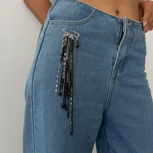 Vue détaillée d'une broche épingle à nourrice à pompons de perles noires sur un jean bleu.