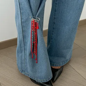 Détail d'une épingle de sûreté à la mode avec des glands en perles rouges sur jeans.