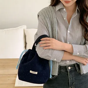 Detail view of a navy blue woolen drawstring bag with white polka dots held by a model