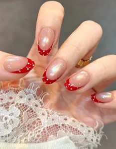 Detailed macro view of short oval press-on nails with red French tips and polka dots.