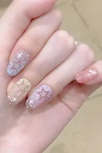 Detail shot of short oval press-on nails with star patterns and pink gradient.