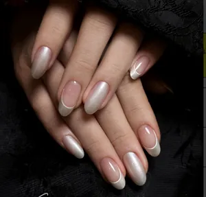 Detail showing pearlescent and French tip oval press-on nails on dark textured fabric.