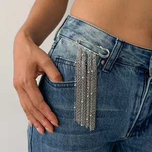 Detailansicht einer silbernen Sicherheitsnadel-Brosche mit Quastenketten auf Jeans.