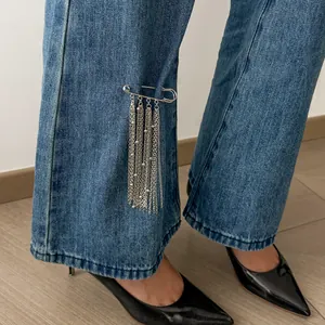 Detailaufnahme einer silbernen Quastenkette-Sicherheitsnadel an einer blauen Jeanshose