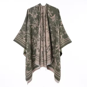 Detailed view of reversible olive green poncho with floral bird pattern and fringe.