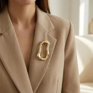 Primer plano de un broche dorado abstracto de acero en una chaqueta beige minimalista elegante