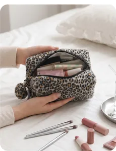 Large leopard print plush cosmetic bag with pom-pom charm held in hands for daily storage