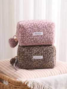 Soft leopard print plush cosmetic bags in pink and brown, stacked on a cozy wicker stool.
