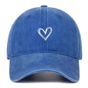 Detailopname van een blauwe gewassen denim baseballpet met witte hartborduring.