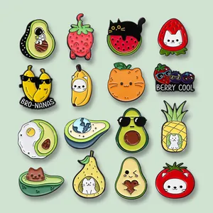 Variedad de lindos pines de esmalte con diseños de frutas y gatos sobre un fondo verde suave