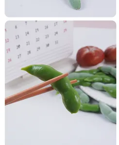Detailed view of a simulated PVC edamame pod held by wooden chopsticks with realistic texture.
