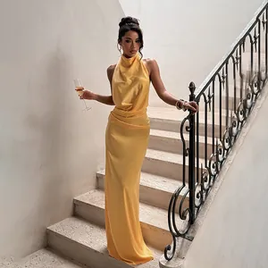 Robe de soirée élégante licou en satin jaune dos nu pour femme posée sur un escalier