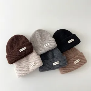 Detailed view of various colored knitted winter beanies for children with small cloth patches.
