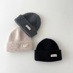 Detailed view of three warm baby knitted beanies in grey, beige, and black colors.