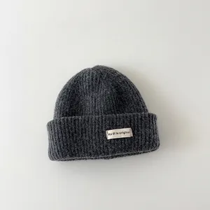 Close-up detail of a dark grey kids' knitted beanie featuring a fabric patch label.