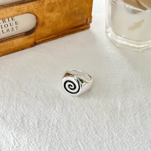 Close-up detail of silver-colored open ring featuring a black enamel spiral design